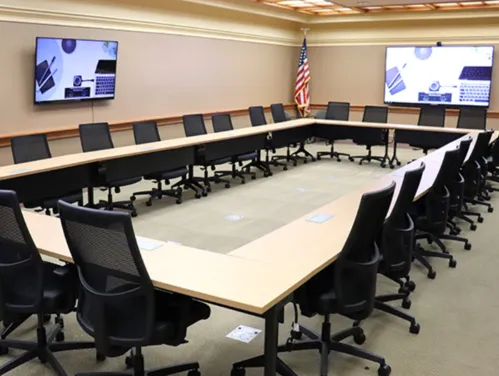 Interior of the Forrest Spaulding Conference Room 310, showing tables and chairs arranged in a rectangle with two wall mounted video monitors.