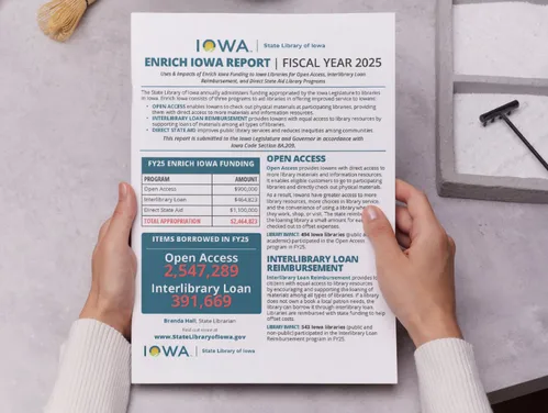 Hands on a tabletop holding a print copy of the Enrich Iowa Legislative Report.