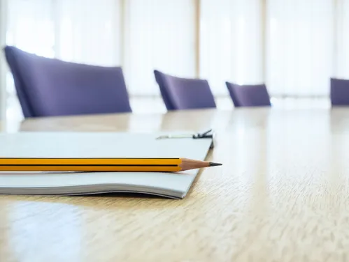Empty boardroom with closeup of pad of paper and pencil on tabletop.