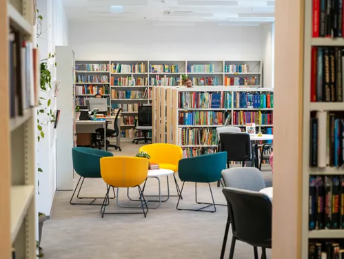 Interior of a library with shelves of books, a seating area and computer desk.