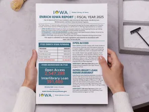 Hands on a tabletop holding a print copy of the Enrich Iowa Legislative Report.