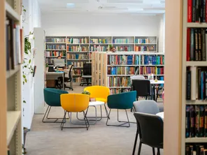 Interior of a library with shelves of books, a seating area and computer desk.