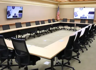 Interior of the Forrest Spaulding Conference Room 310, showing tables and chairs arranged in a rectangle with two wall mounted video monitors.
