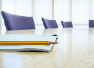 Empty boardroom with closeup of pad of paper and pencil on tabletop.