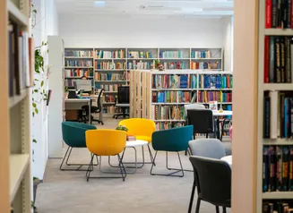Interior of a library with shelves of books, a seating area and computer desk.